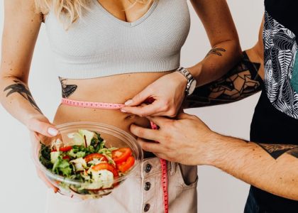 A couple measuring waistline with a tape and holding a fresh salad bowl, focusing on fitness and weight loss.