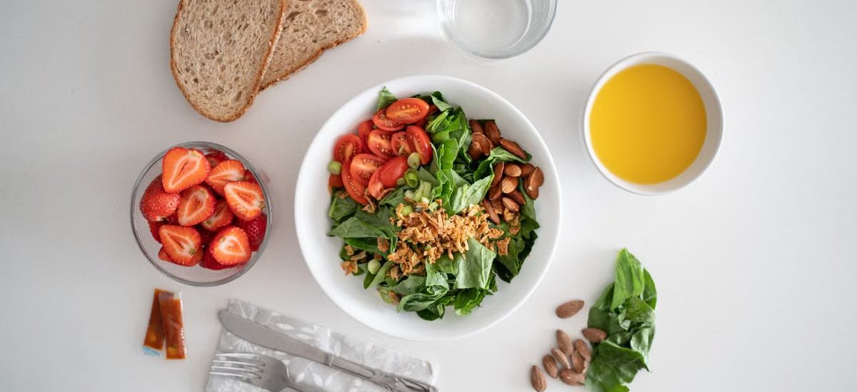 Top view of a healthy salad and fresh ingredients with bread and juice on a white surface.