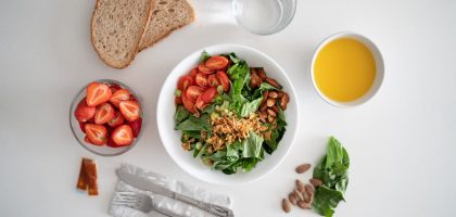 Top view of a healthy salad and fresh ingredients with bread and juice on a white surface.
