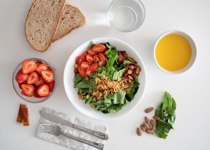 Top view of a healthy salad and fresh ingredients with bread and juice on a white surface.