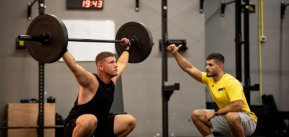 Man lifting weights under coach supervision in a gym setting, focusing on strength training.