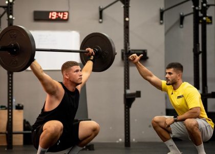 Man lifting weights under coach supervision in a gym setting, focusing on strength training.